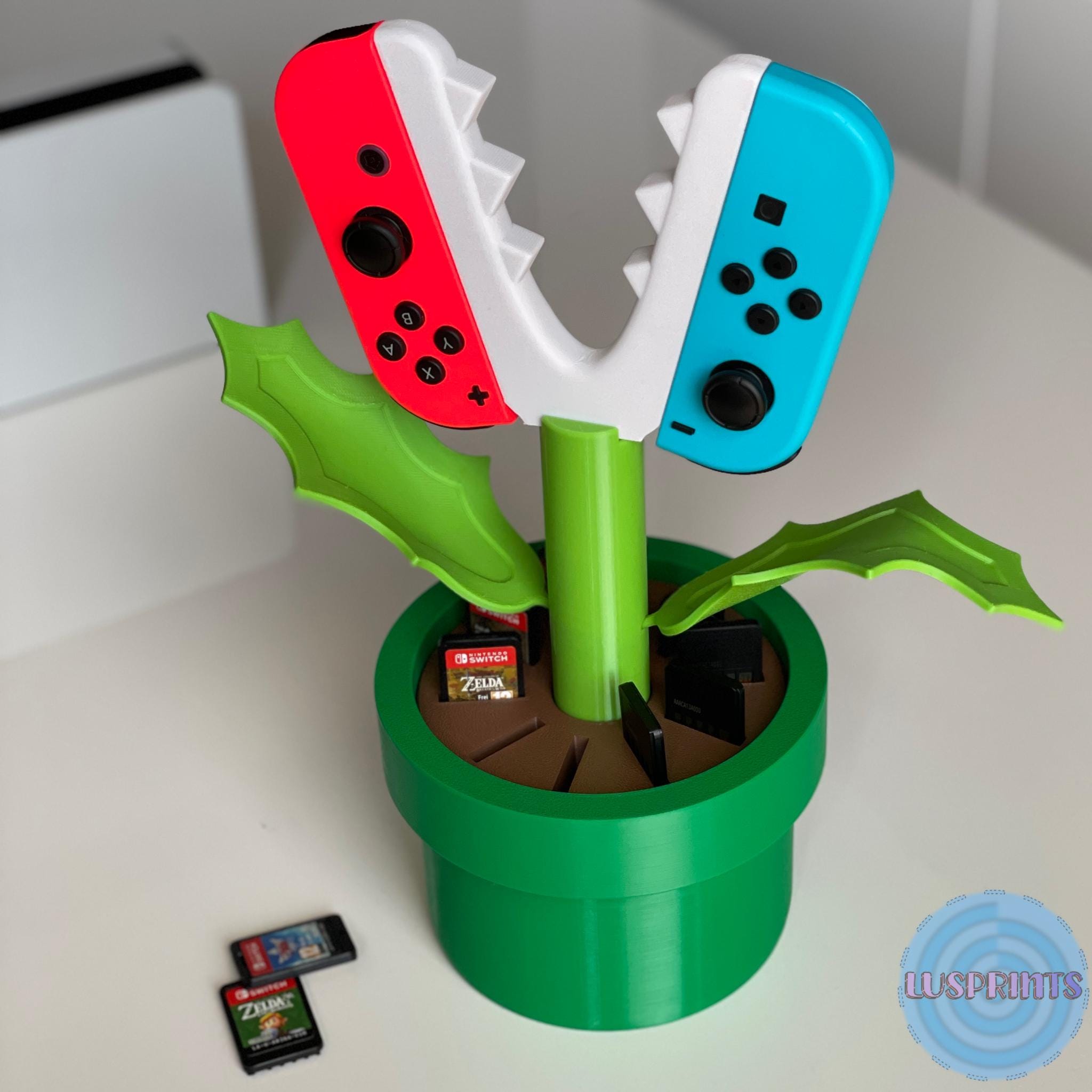 3D-gedruckter Piranha Plant Ständer mit eingesetzten roten und blauen Joy-Cons und Switch-Spielekarten im Topf.